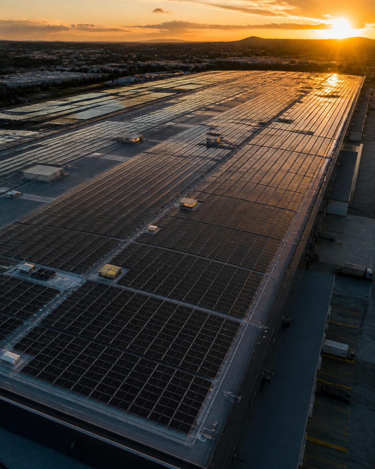 Massive industrial warehouse rooftop covered in solar panels at sunset